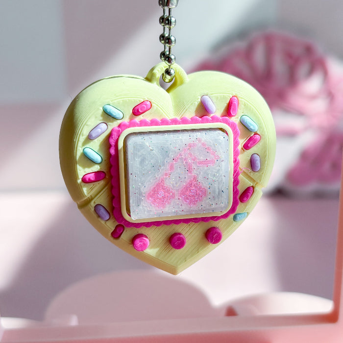 Heart-shaped keychain with colorful decorations on a pink background