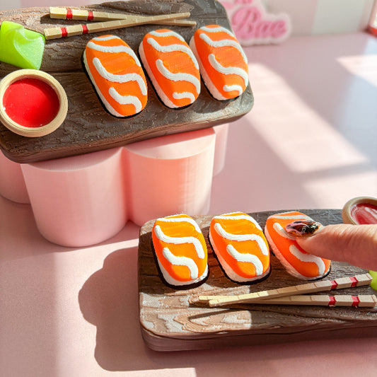Decorative fidget clicker haped like salmon sushi on a wooden board with a hand holding one cookie.