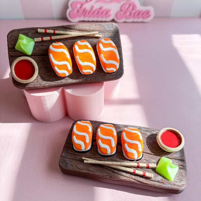 Decorative fidget clicker haped like salmon sushi on a wooden board with a hand holding one cookie.