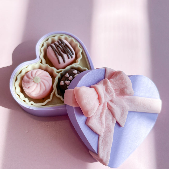 Sweetheart_Fidget_Clicker Heart-shaped box with pastel-colored treats and a pink bow on a light pink background