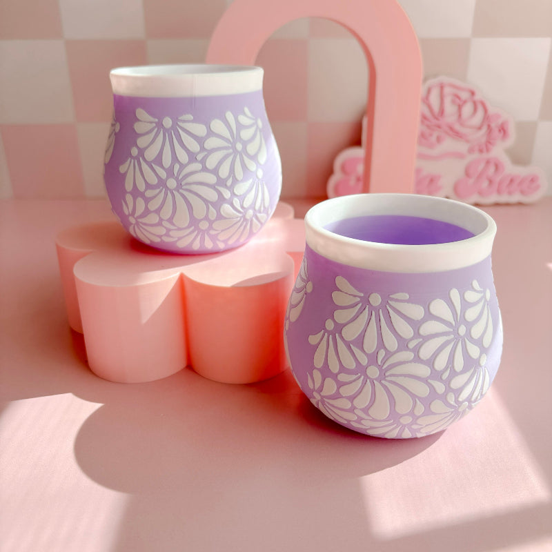 Two purple 3D Printed cups with white floral patterns on a pink surface.