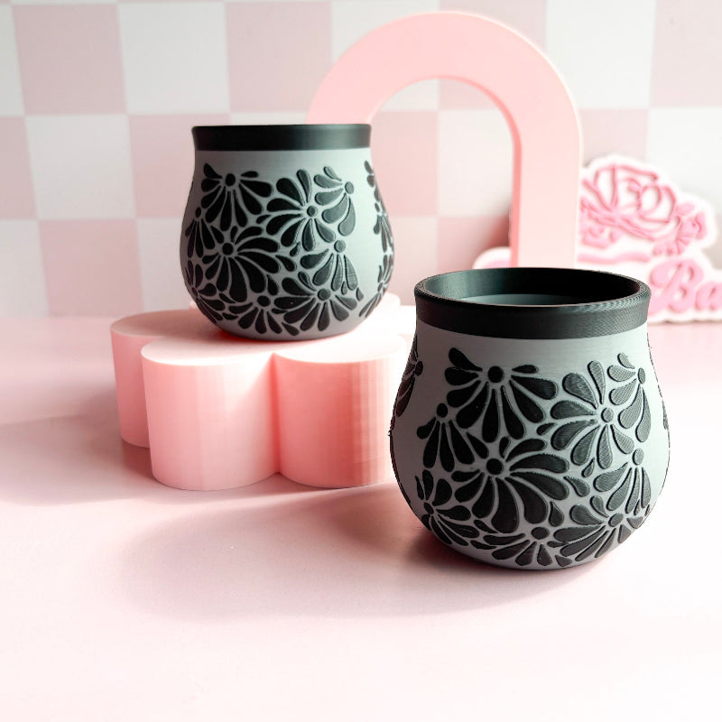 Two decorative 3D Printed vases with floral patterns on a pink and white checkered background