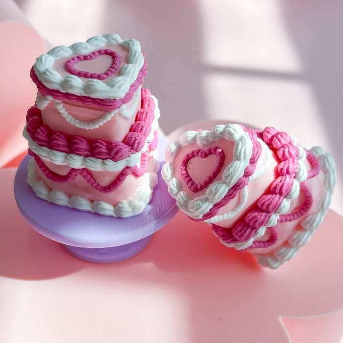 Pink and white cake-shaped fidget toy with heart designs on a pink background