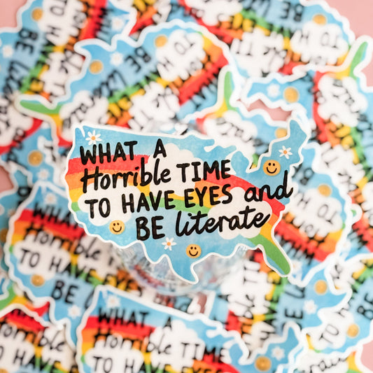 Colorful sticker with text 'What a horrible time to have eyes and be literate' on a multicolored background.