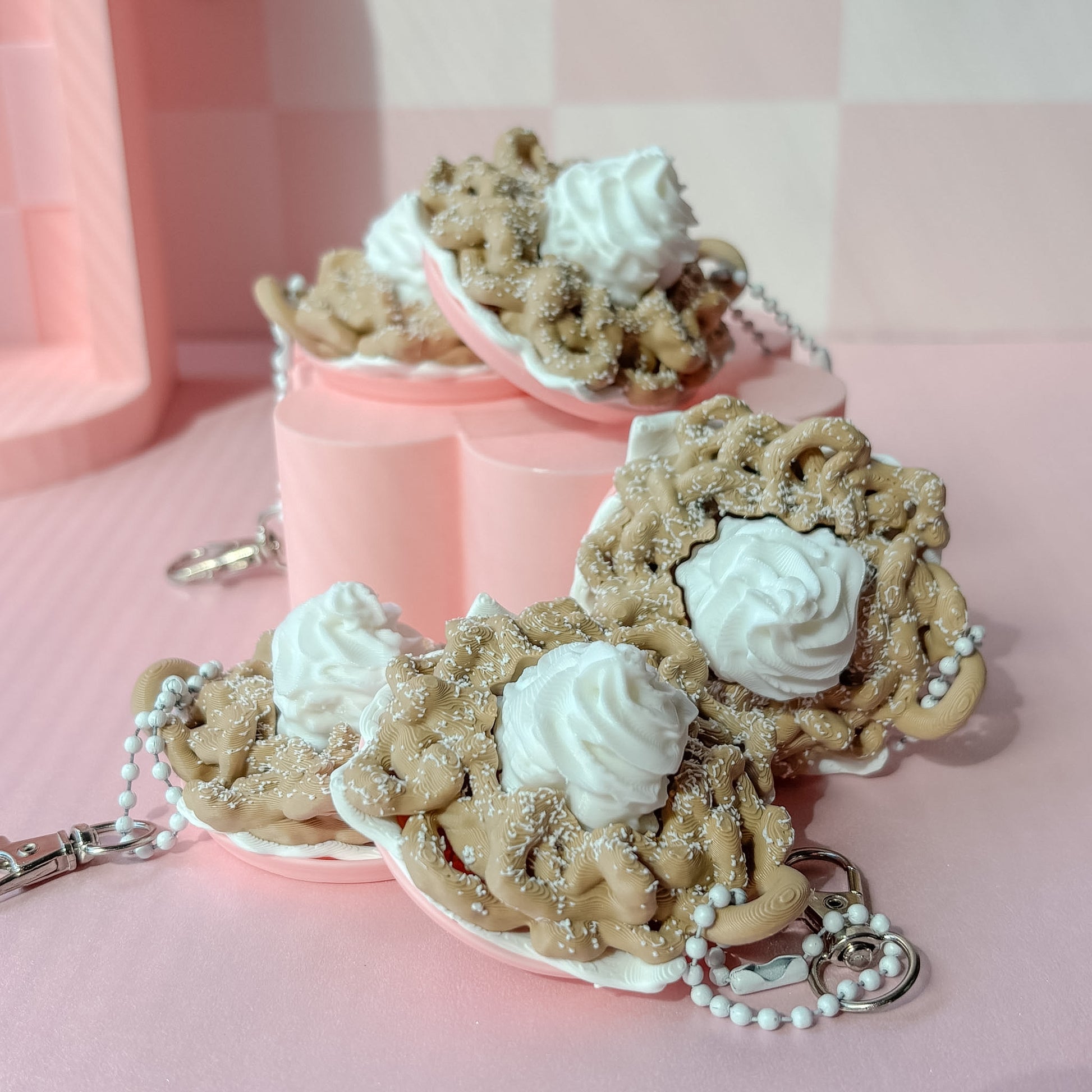 Keychains shaped like funnel cake with white frosting on a pink checkered background