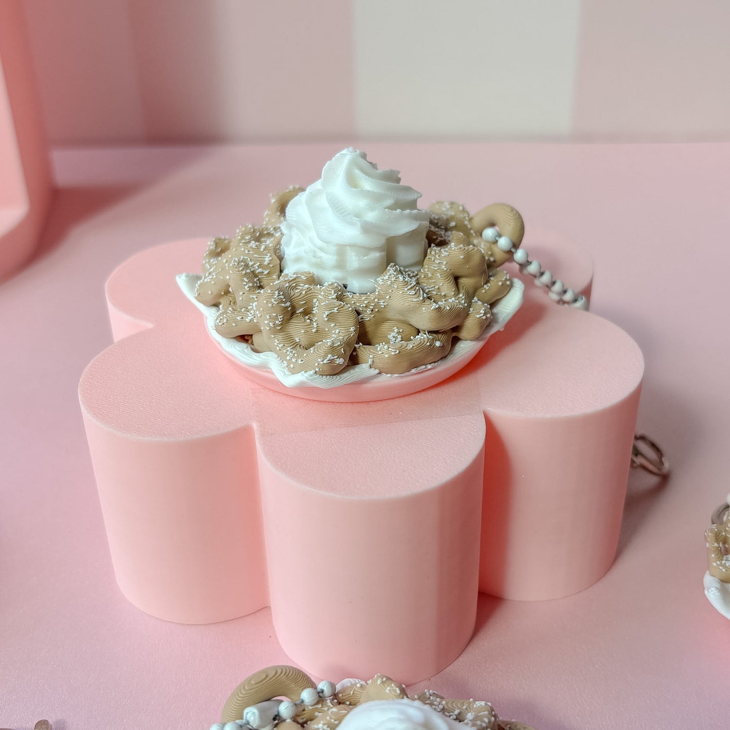 Keychains shaped like funnel cake with white frosting on a pink checkered background