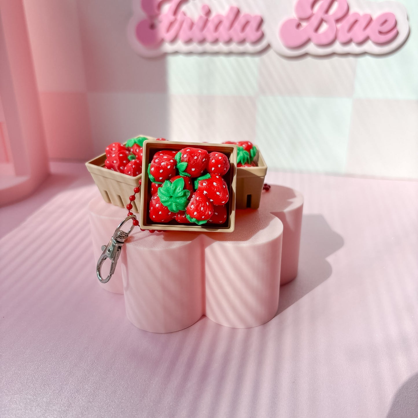 Strawberry-themed fidget clicker on pink stands with 'Frida Bae' branding in the background