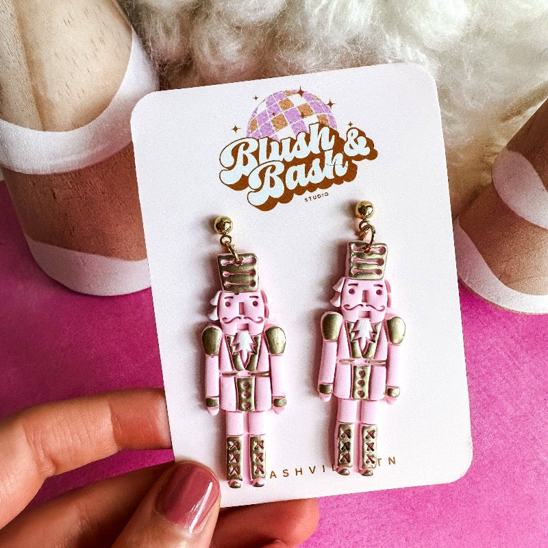 Put a whimsical spin on your look with our Hand-Painted Pink Nutcracker Dangle Earrings! These playful pieces bring a touch of artistic charm to any ensemble. Crafted with care, these earrings have all the details you need with a hand-painted nutcracker motif that'll keep your style silly and sassy.